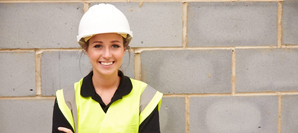 Female construction worker standing against brick wall
