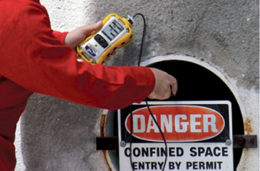 A man doing a gas test atmospheres training course with a equipment of gas testing and warning board near to it.