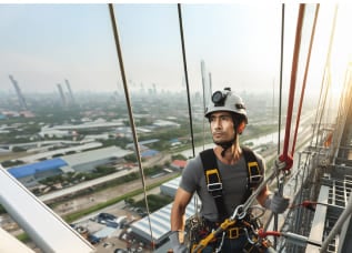 A construction worker is standing at the top of the building wearing a safety harness and a safety line working at a high place.